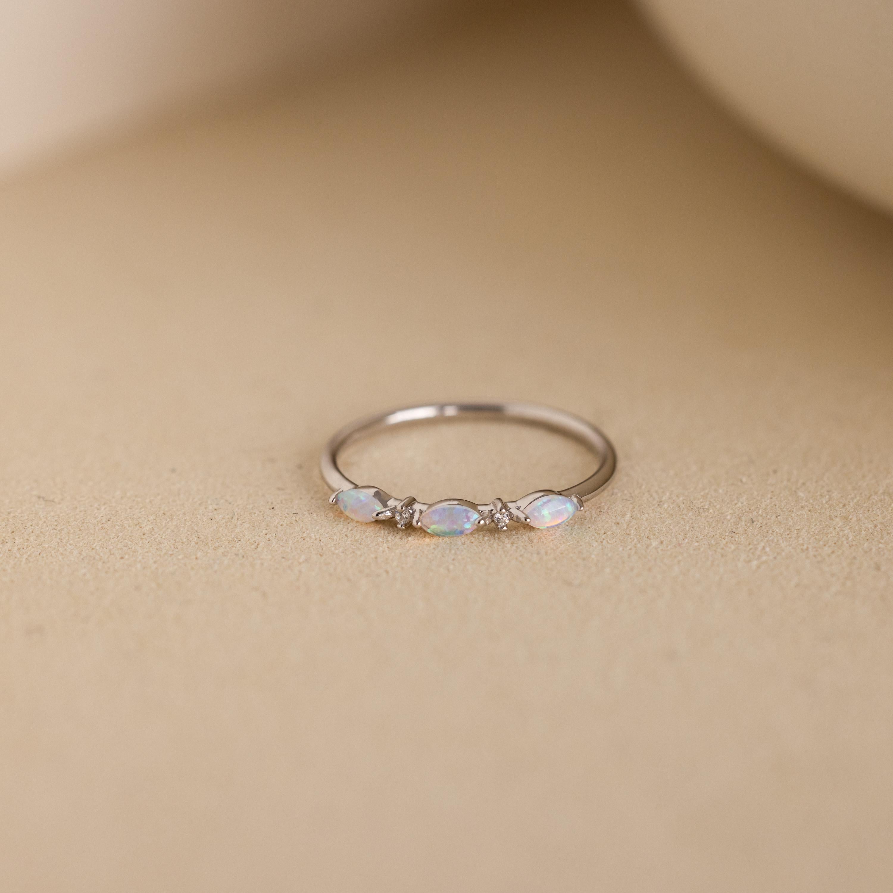 A close-up of the Alessia Trio Opal Ring in silver, featuring three marquise-cut opals accented with tiny diamonds on a slim silver band, displayed against a neutral beige background.