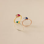 Three elegant rings with vibrant gemstones—including the Toi et Moi Pear Birthstone Ring—are arranged upright on a neutral beige background, making them a perfect romantic gift.