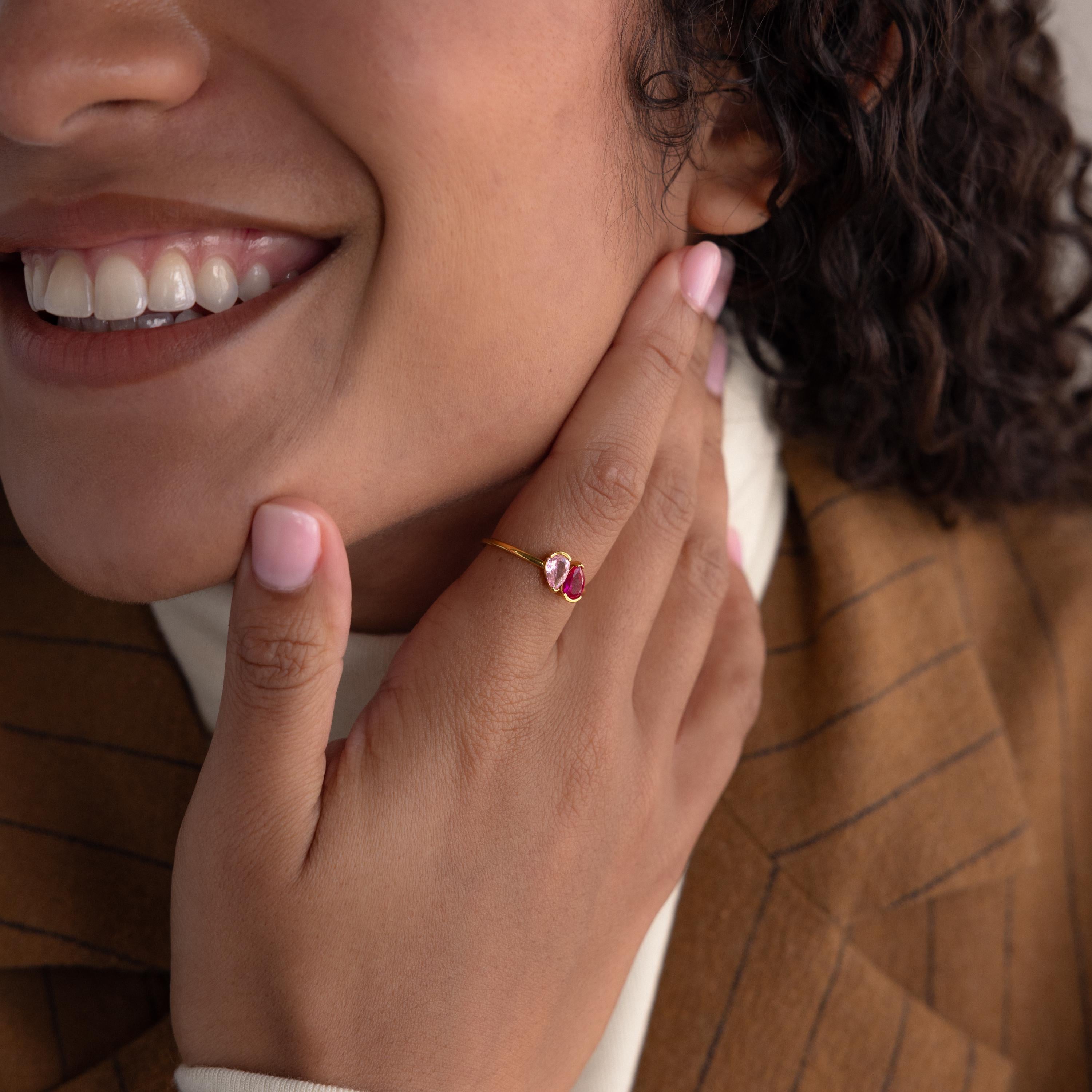 A woman smiles, touching her face with manicured nails, wearing the Toi et Moi Pear Birthstone Ring featuring a pink gemstone—an ideal romantic gift.