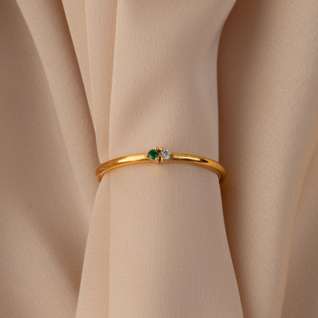 Gold bangle with green and white gemstones displayed on beige fabric—pair it with the Mini Toi et Moi Birthstone Ring for a timeless look.