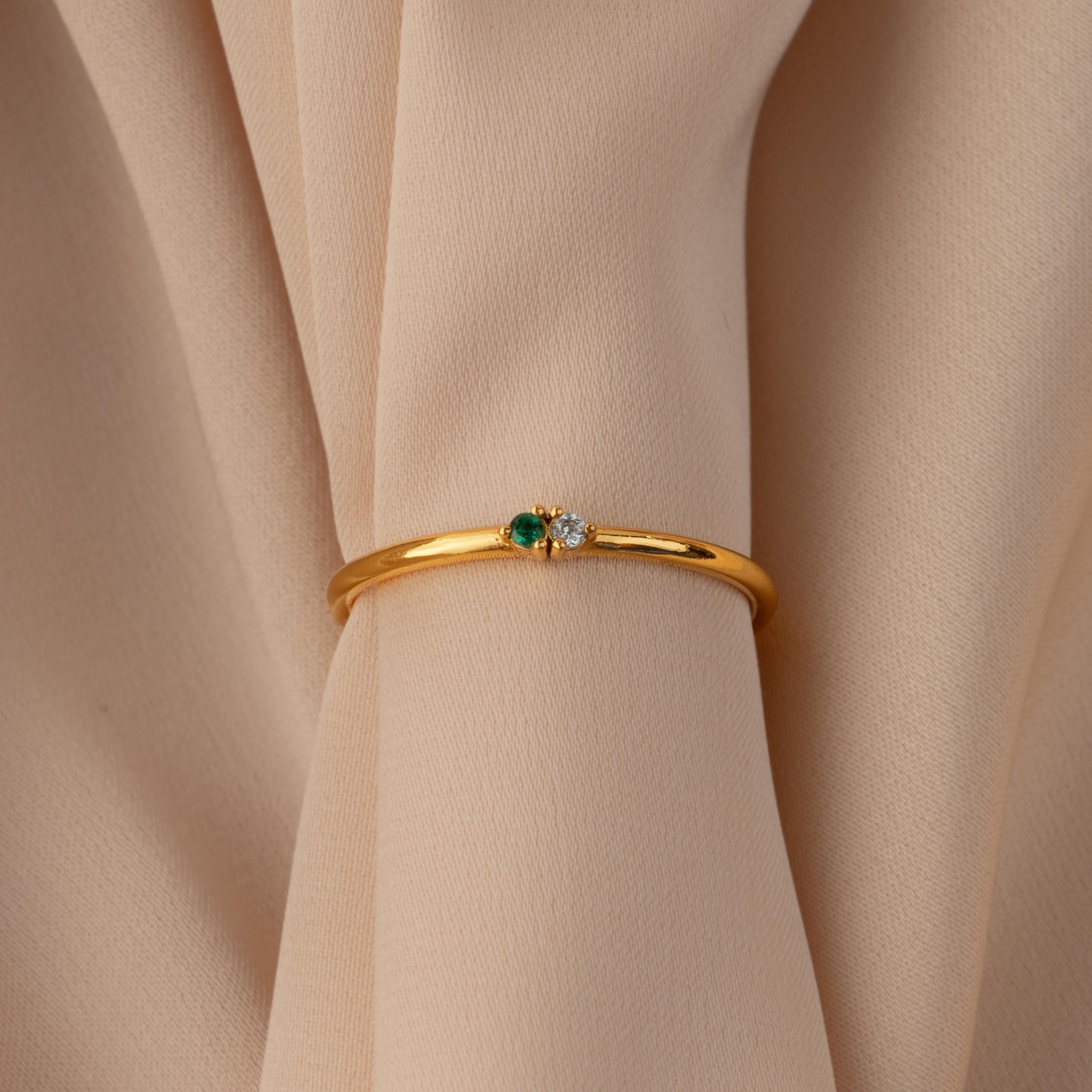 Gold bangle with green and white gemstones displayed on beige fabric—pair it with the Mini Toi et Moi Birthstone Ring for a timeless look.