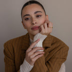 A woman wearing a brown pinstripe blazer and the Mini Toi et Moi Birthstone Ring rests her head on her hand, appearing thoughtful.