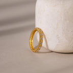 The Diamond Eternity Ring features sparkling diamonds set in gold and rests against a textured, light stone—an elegant, stackable piece ideal for any occasion.