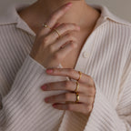A person in a cream ribbed shirt wears several gold rings, including the Diamond Eternity Ring, stacked on their fingers with hands near their face.