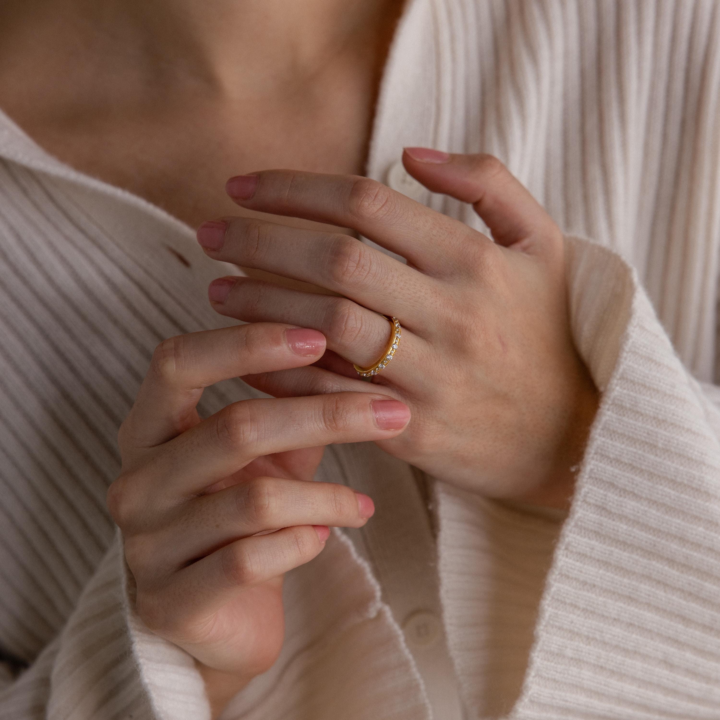 A person in a ribbed cream shirt uses both hands to adjust a Diamond Eternity Ring on their finger.
