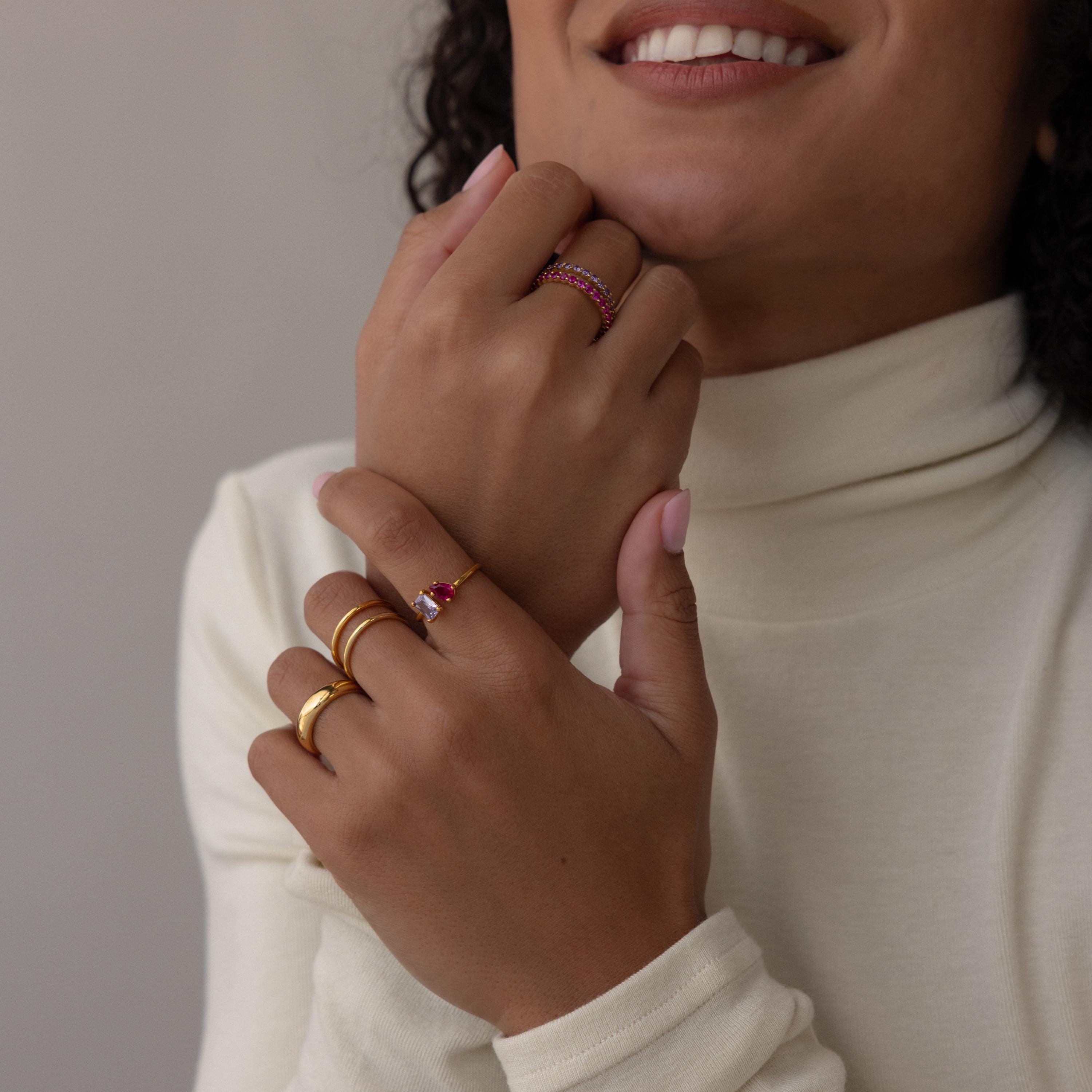 Woman in a cream turtleneck smiles and displays her hands adorned with gold rings, including a stacking birthstone ring and the elegant Open Toi et Moi Birthstone Ring.