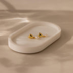 Two Heart Pearl Drop Earrings, featuring gold heart-shaped designs and delicate pearls, are displayed on a white oval ceramic dish.