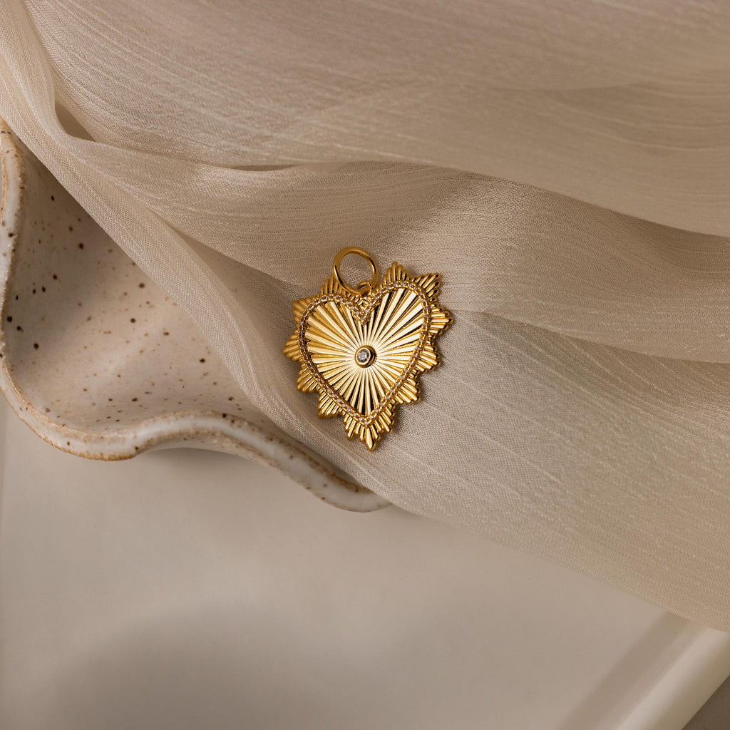 Gold ribbed Diamond Heart Pendant with a central diamond and sunburst detailing, resting on soft fabric.