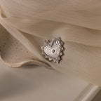 White gold ribbed heart charm with a central diamond and sunburst detailing, resting on soft fabric