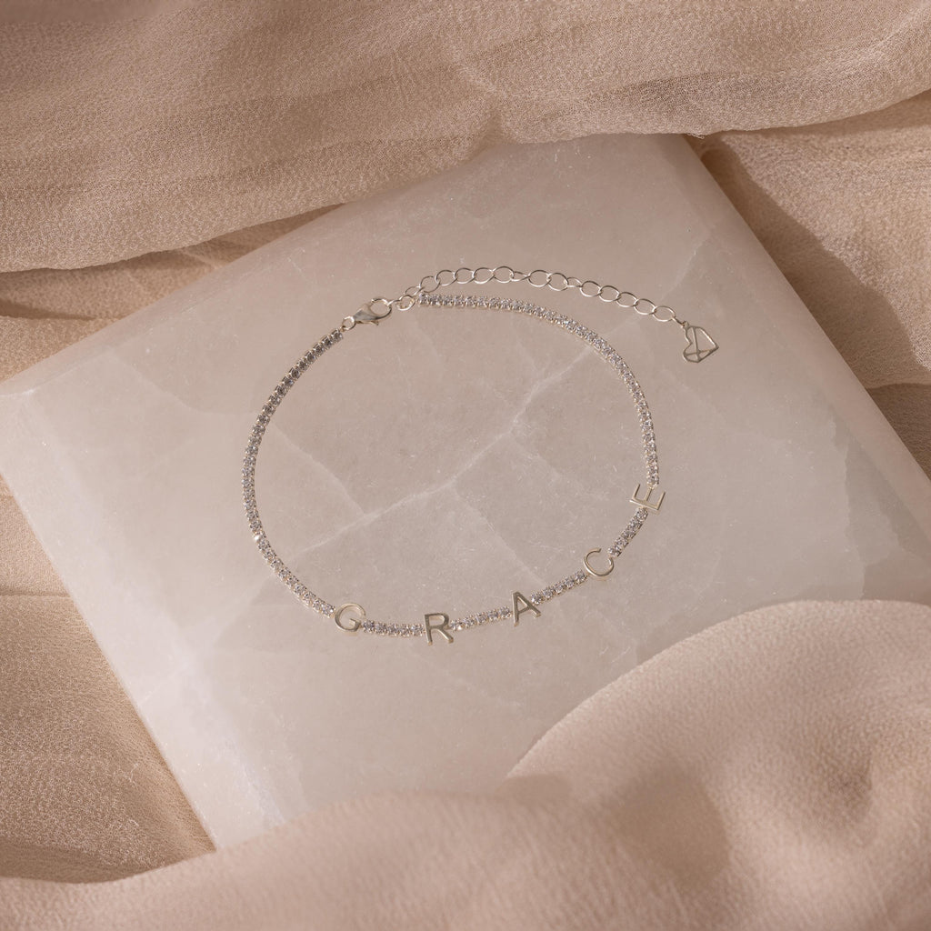 Elegant silver Mama Tennis Letter Bracelet on a soft beige fabric and marble-like surface—perfect for gifting or adding to your personalized jewelry collection.