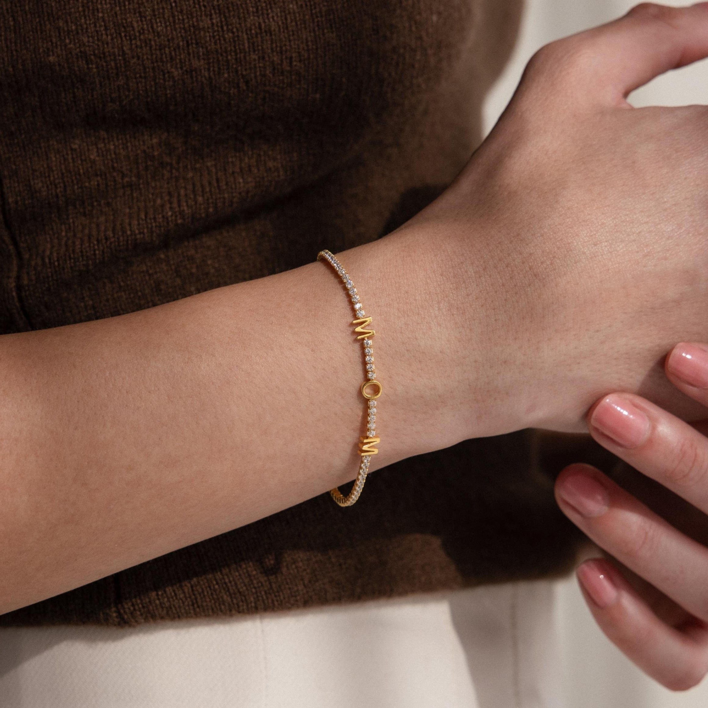 The Mama Tennis Letter Bracelet—an elegant customized gold bracelet adorned with pearls and gems, ideal for gifting and beautifully worn on the wrist—makes a stunning statement piece.