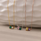 The Toi et Moi Emerald Birthstone Necklace, one of three delicate chain necklaces, features a colorful gemstone pendant displayed against a textured white background.