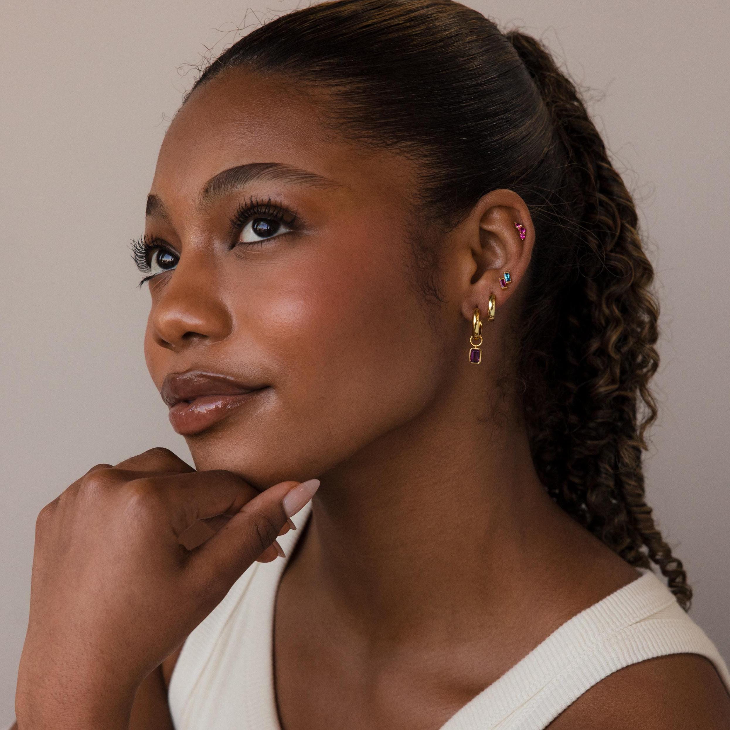 Woman with a curly ponytail in a white top, resting her chin on her hand and looking upward, wearing Duo Baguette Birthstone Studs.
