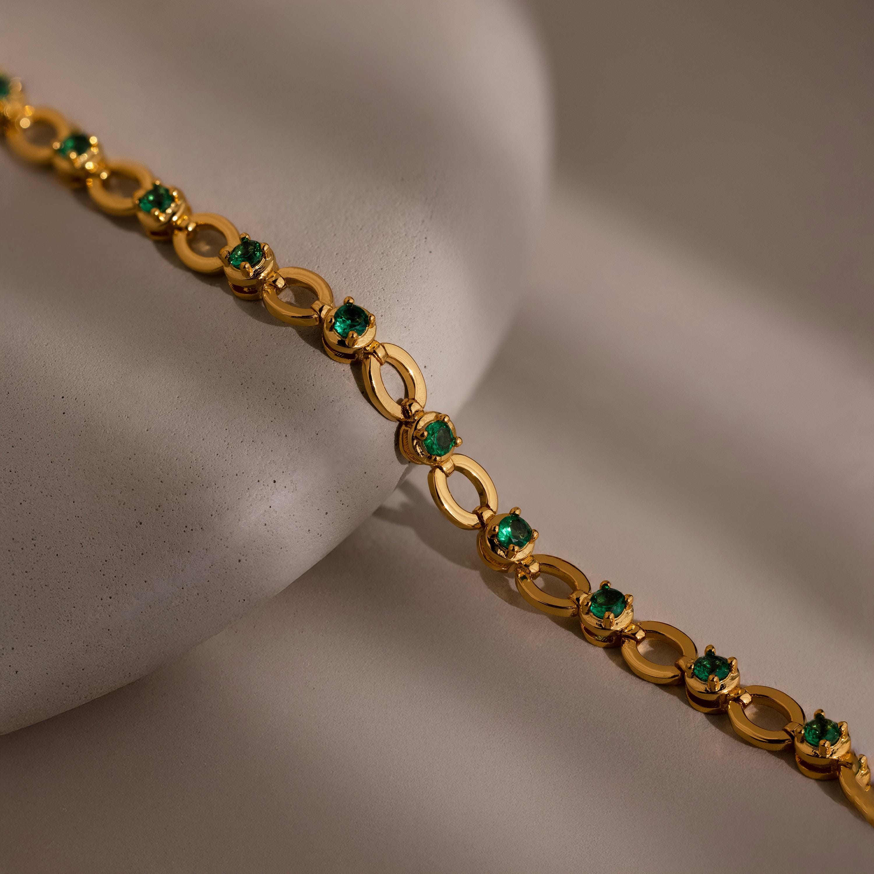 Emerald Chain Tennis Bracelet showcased on a smooth, light beige surface.