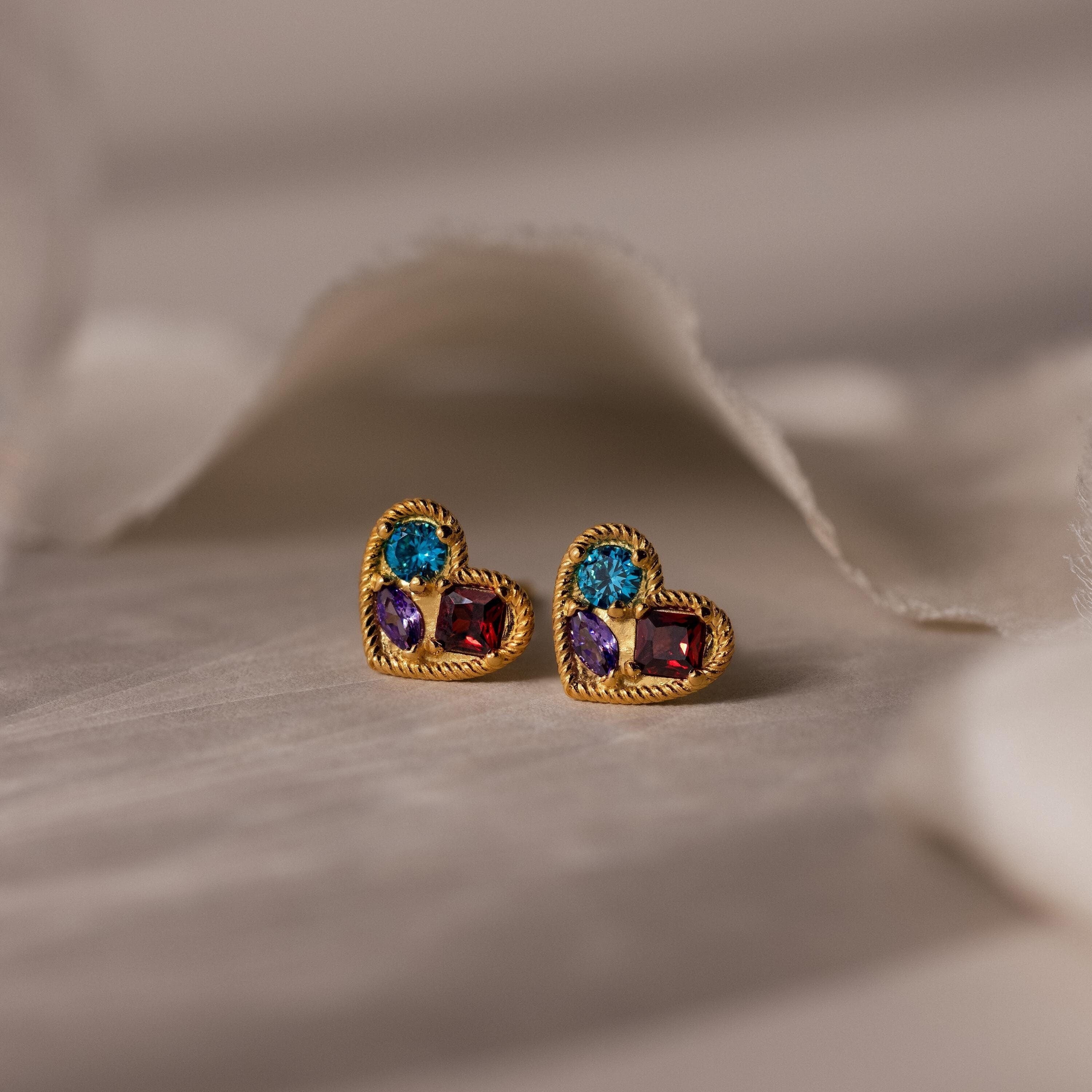 Mixed Birthstone Heart Studs with customizable gemstones, shown on a soft, neutral fabric background.