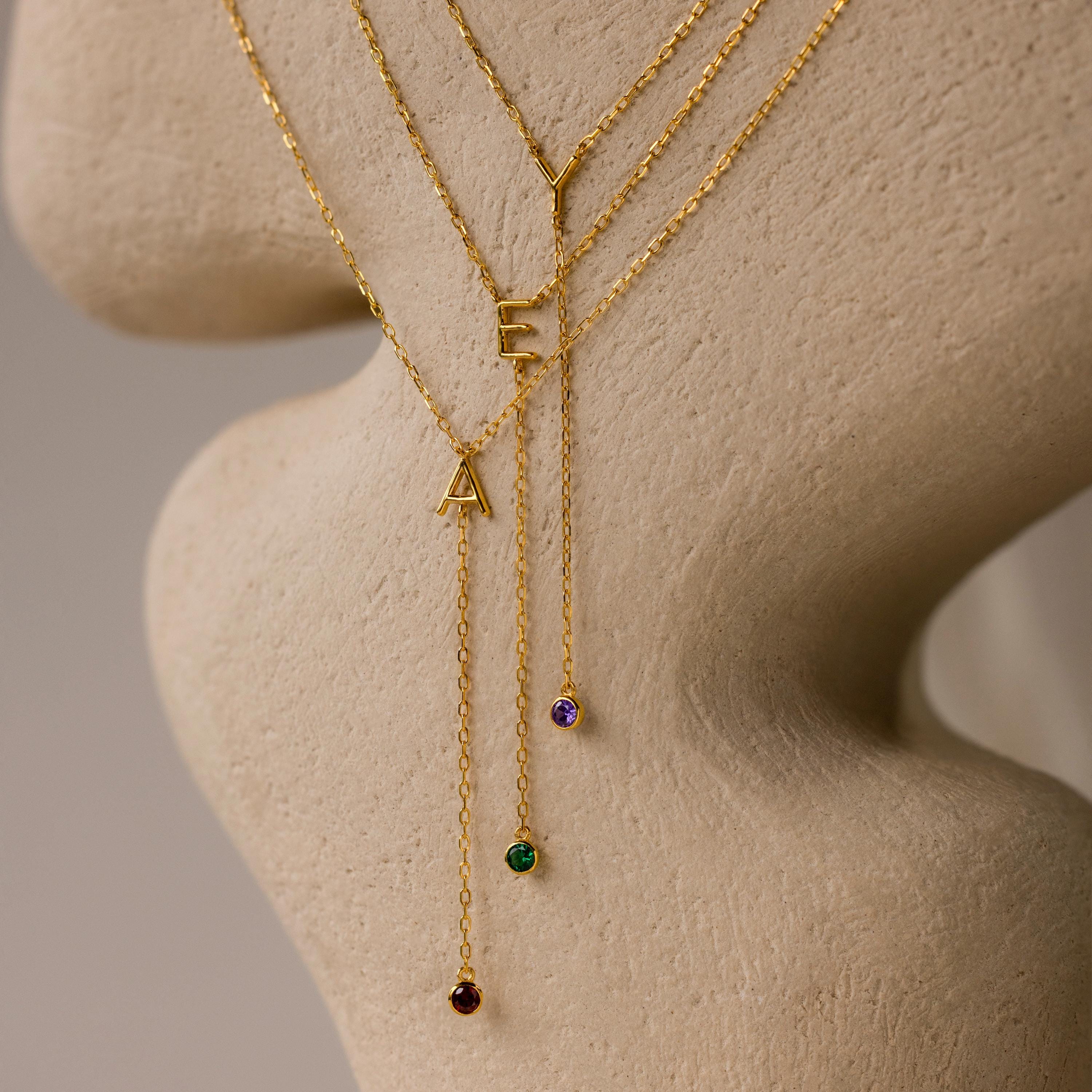 The Initial Birthstone Lariat Necklace features gold lariats with A, E, or Y letter pendants, each finished with a colored gemstone—ideal as personalized jewelry gifts.