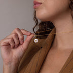 Woman wearing a brown blazer holds the Pearl Initial Pendant Necklace, featuring a personalized round pendant with the letter K.