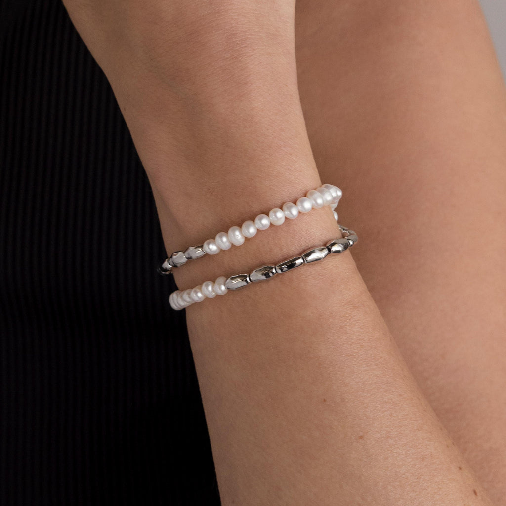 A wrist styled with the Duo Beaded Pearl Bracelet—featuring layered pearls and small silver beads—contrasts elegantly against a black sleeve.
