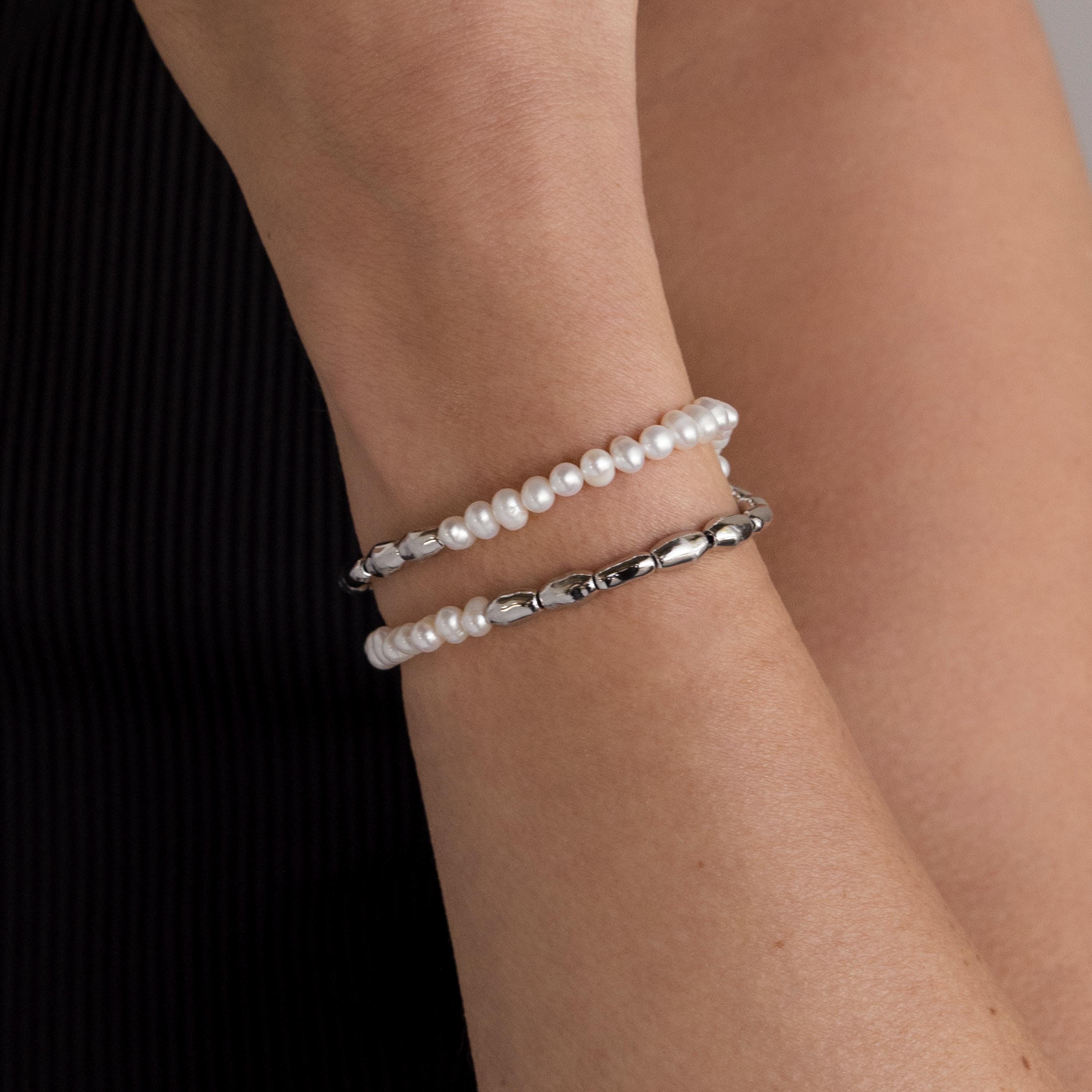 A wrist styled with the Duo Beaded Pearl Bracelet—featuring layered pearls and small silver beads—contrasts elegantly against a black sleeve.