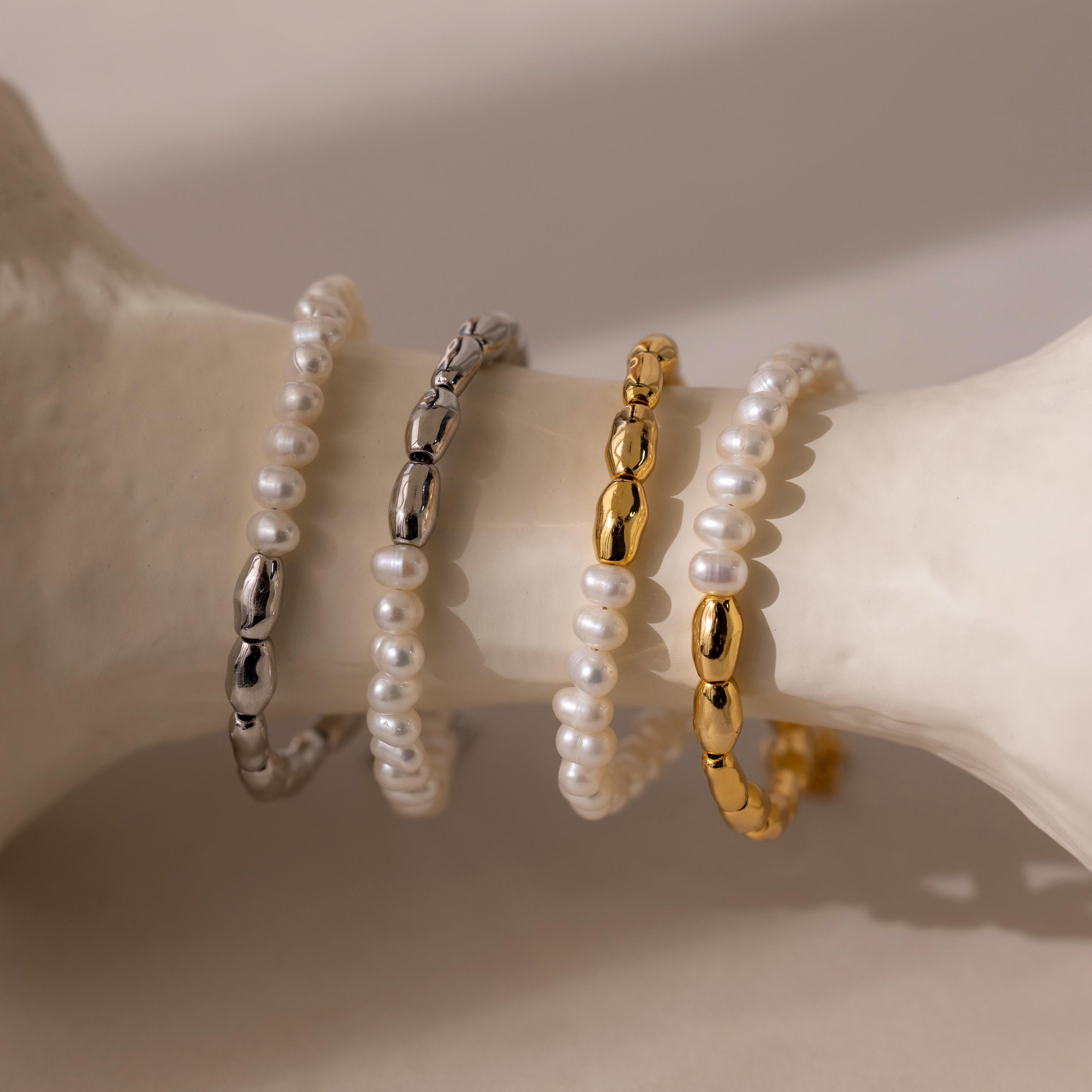 The Duo Beaded Pearl Bracelet, featuring layers of pearls and metallic beads, rests on a white curved surface in soft lighting.