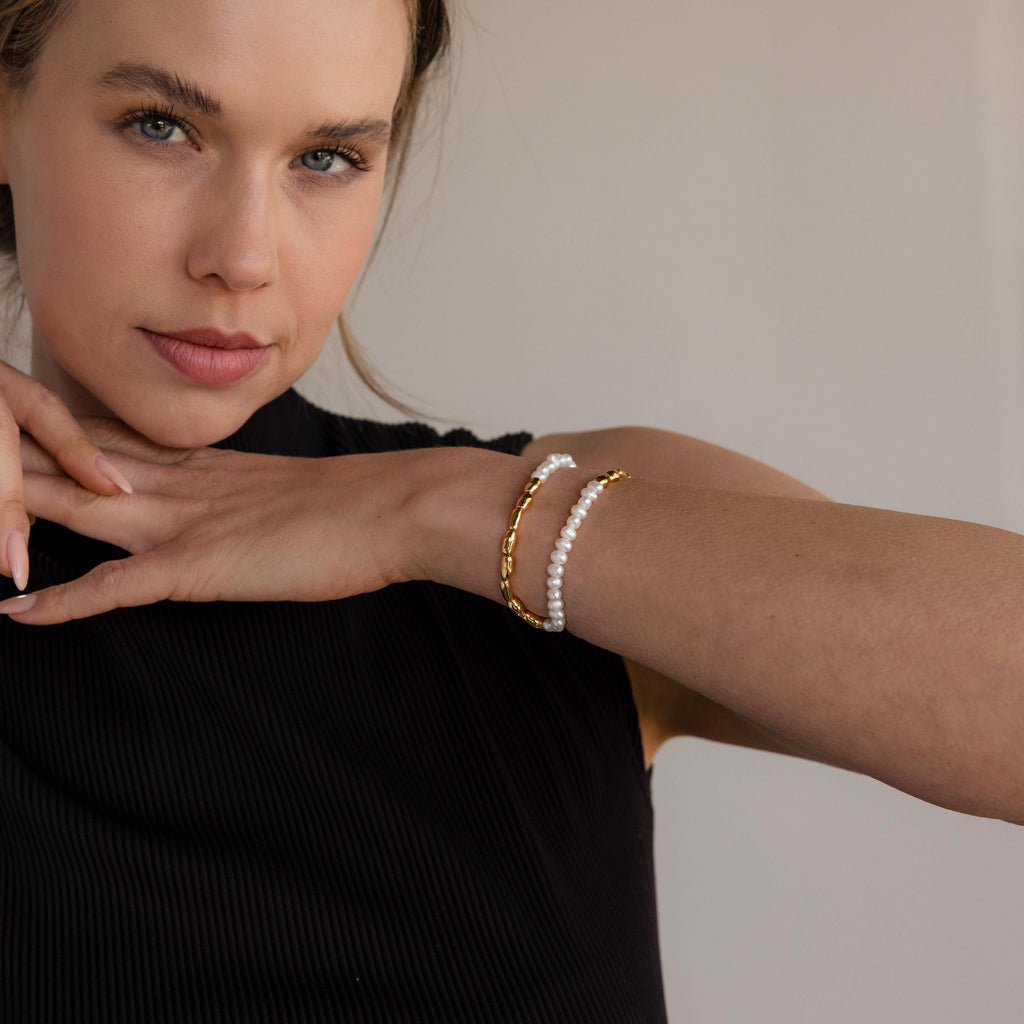 A woman in a black top wears the Duo Beaded Pearl Bracelet, resting her hands on her shoulder and gazing at the camera.