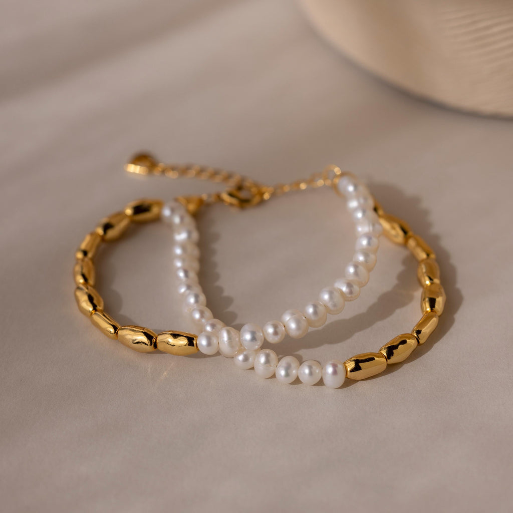 The Duo Beaded Pearl Bracelet, featuring gold chain and beaded pearls, is displayed on a soft beige surface—ideal for creating a chic layered bracelet look.