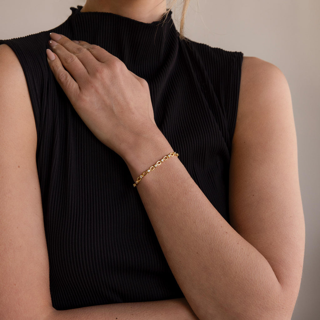 A woman in a sleeveless black top wears the Diamond Chain Tennis Bracelet, its sparkling diamonds adorning her wrist as her hand rests gracefully on her chest.