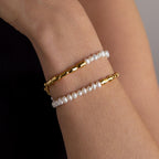 A wrist adorned with the Duo Beaded Pearl Bracelet—featuring one gold beaded layer and one delicate pearl strand—set against a neutral background.