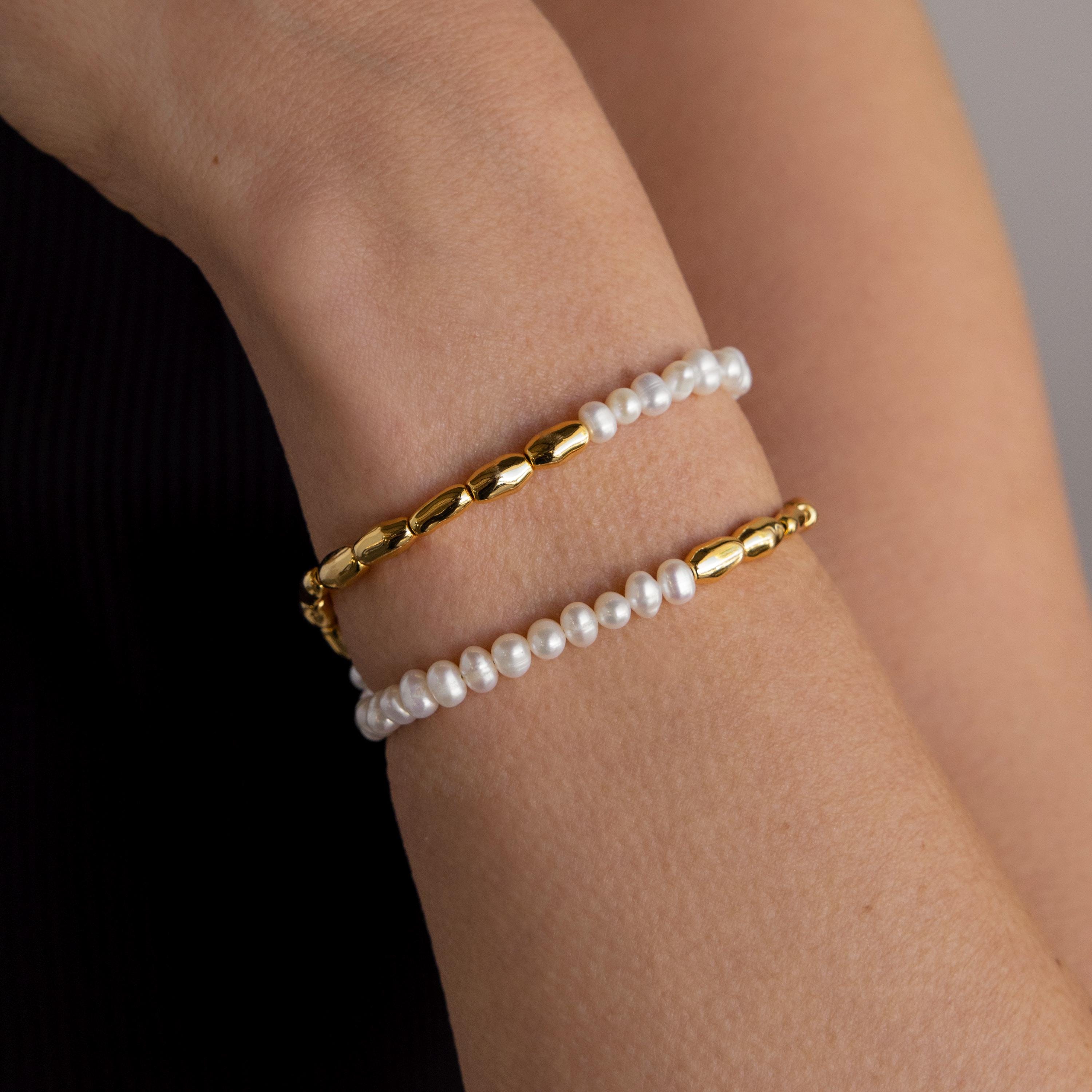 A wrist adorned with the Duo Beaded Pearl Bracelet—featuring one gold beaded layer and one delicate pearl strand—set against a neutral background.