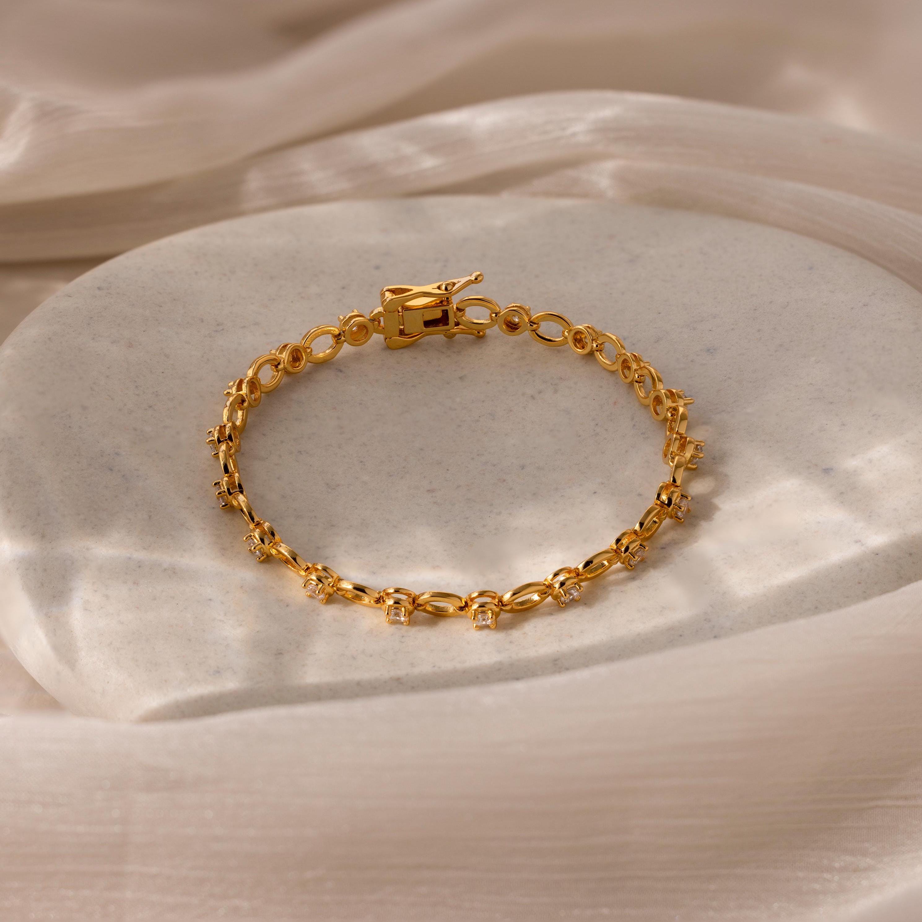 Diamond Chain Tennis Bracelet featuring gold links, displayed on a smooth light stone surface with soft fabric drapes, echoing the timeless elegance of classic tennis bracelets.