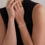 A woman wearing a Diamond Chain Tennis Bracelet with gold links pairs it with gold rings and a black sleeveless top, hands held near her face.