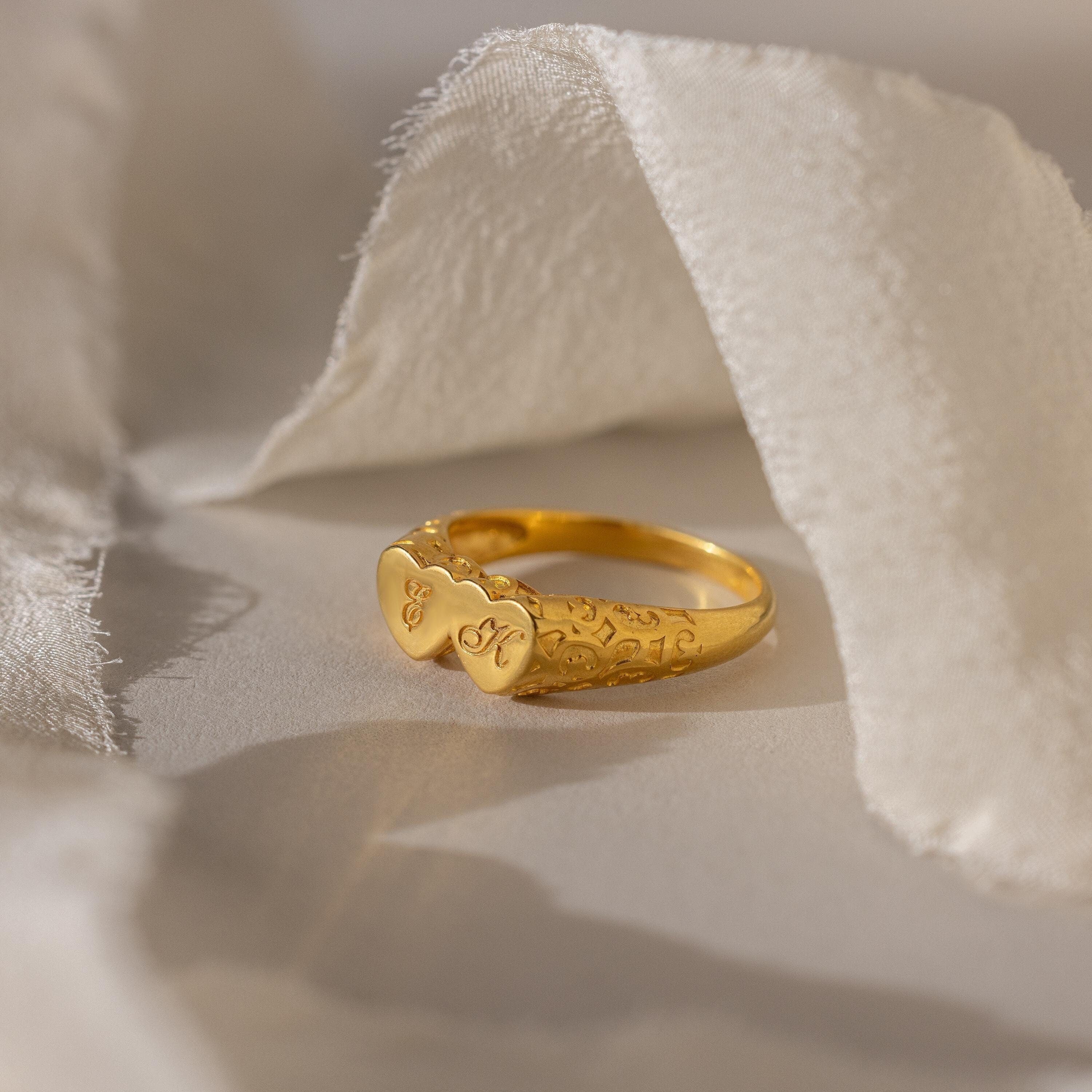 The Duo Initial Heart Ring features two heart shapes engraved with initials, beautifully displayed on soft, white fabric.