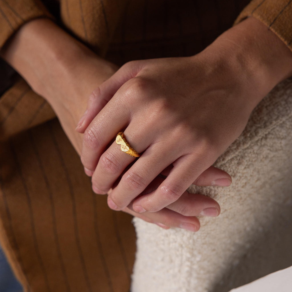 Close-up of hands wearing the Duo Initial Heart Ring with engraved hearts, shown resting on a textured white surface.