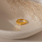 The Duo Initial Heart Ring features engraved details, displayed on a textured, off-white surface with dried grass in the background.