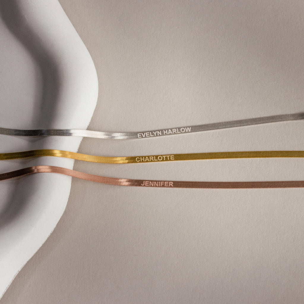 Three satin ribbons labeled EVELYN HARLOW, CHARLOTTE, and JENNIFER on a neutral background evoke the refined charm of the Engraved Herringbone Name Necklace—ideal inspiration for a personalized necklace collection.