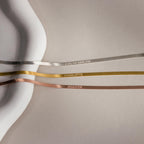 Three satin ribbons labeled EVELYN HARLOW, CHARLOTTE, and JENNIFER on a neutral background evoke the refined charm of the Engraved Herringbone Name Necklace—ideal inspiration for a personalized necklace collection.