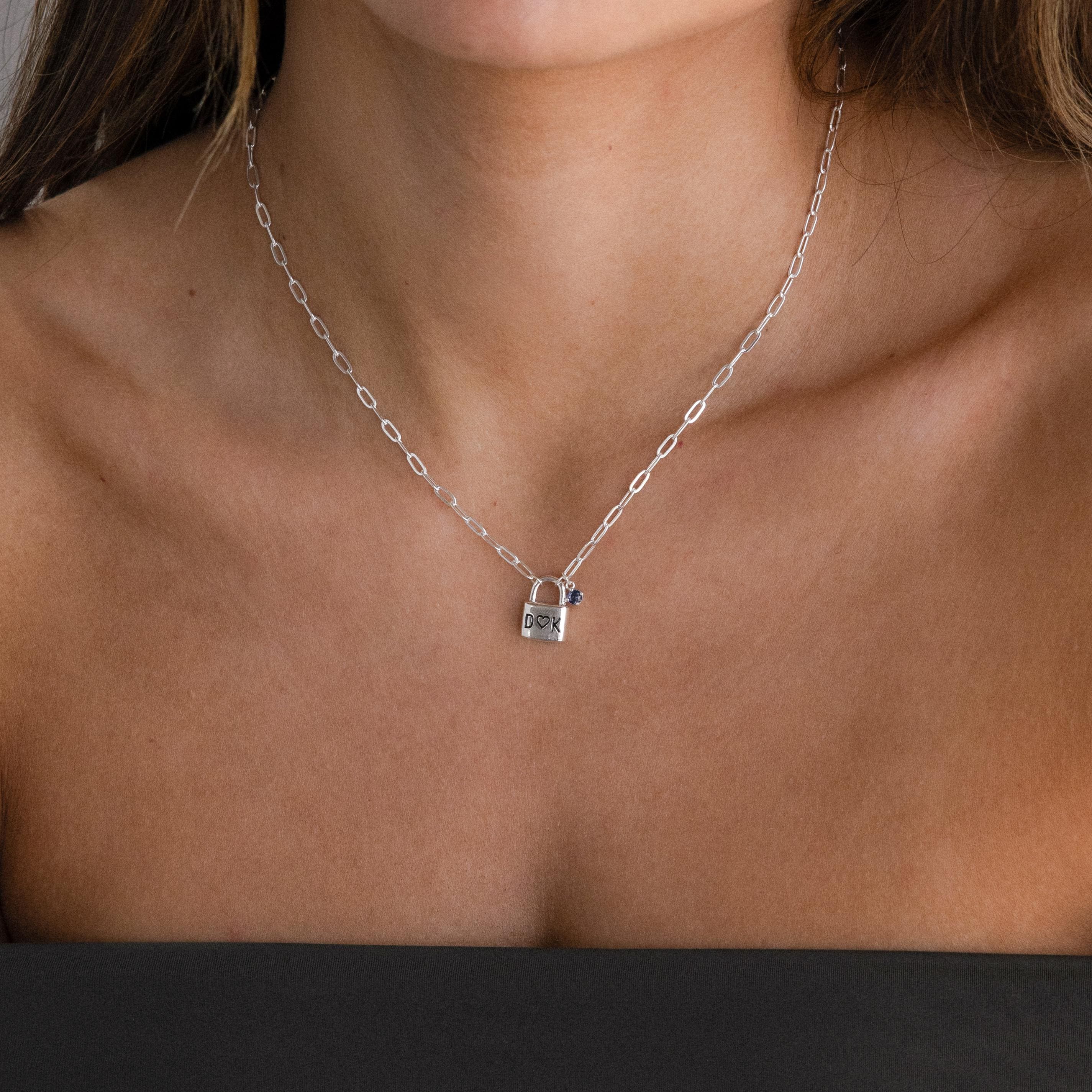 Close-up of a woman wearing the Initial Birthstone Padlock Necklace—a silver necklace with a lock-shaped pendant and a small purple gem, ideal as an initial birthstone accessory.