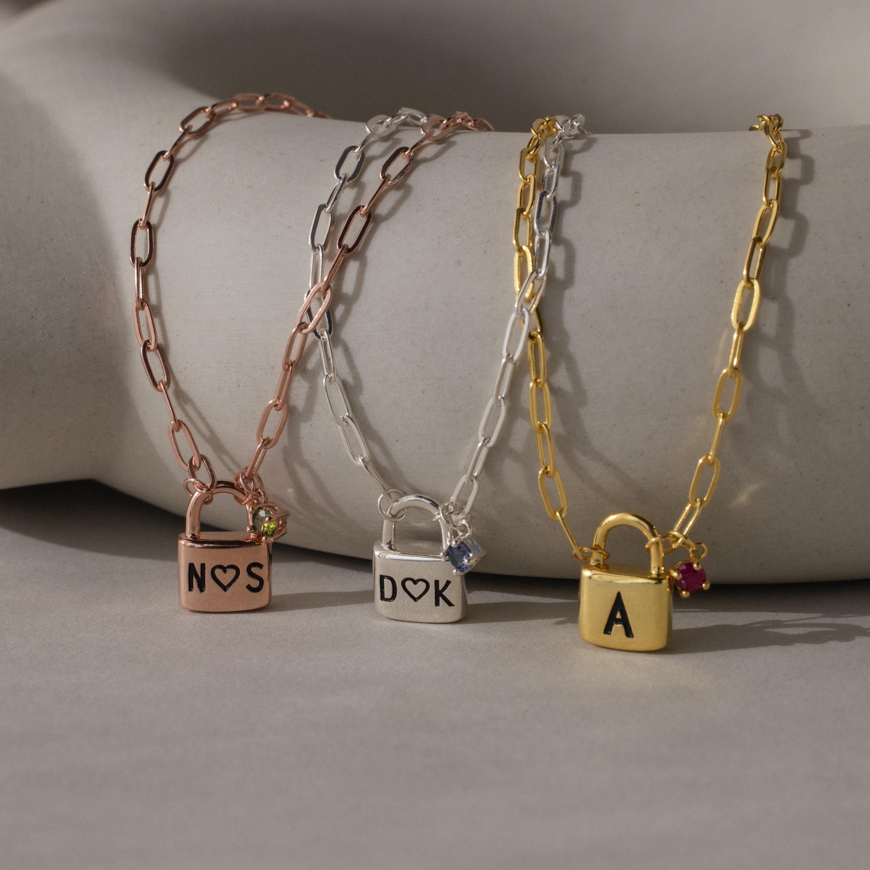 The Initial Birthstone Padlock Necklace set features three chain necklaces, each with a personalized padlock pendant engraved with initials and accented by a birthstone—making the perfect gift.