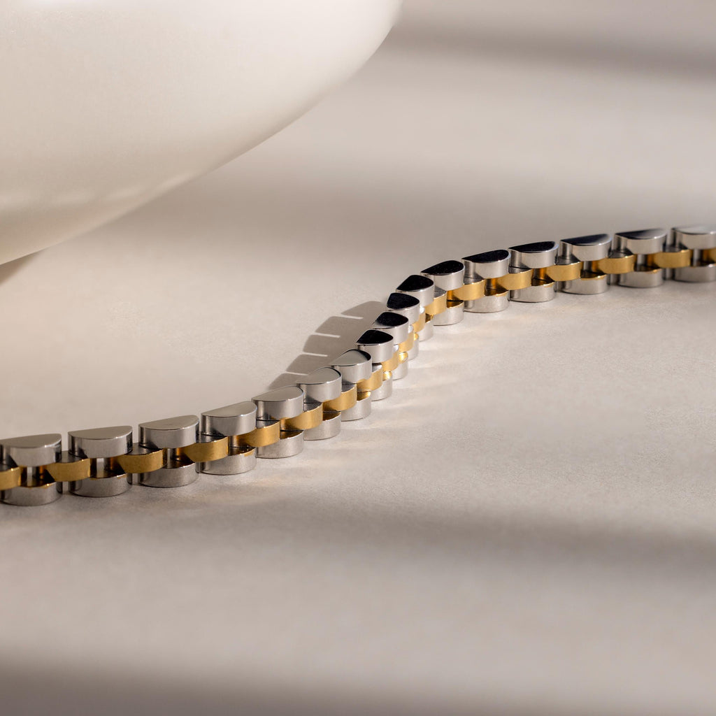 A close-up of the Mixed Metal Link Bracelet showcases its silver and gold design, making it a stylish gift for him. Displayed on a light surface.