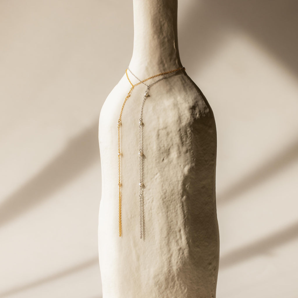 A Pearl Hand Chain Bracelet draped over a textured white vase in soft, natural light, capturing the essence of summer elegance.