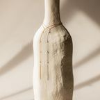 A Pearl Hand Chain Bracelet draped over a textured white vase in soft, natural light, capturing the essence of summer elegance.