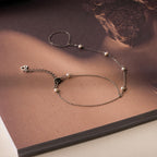 The Pearl Hand Chain Bracelet features small pearls and is displayed on an open book with a soft brown background—an elegant accessory to enhance your summer style.
