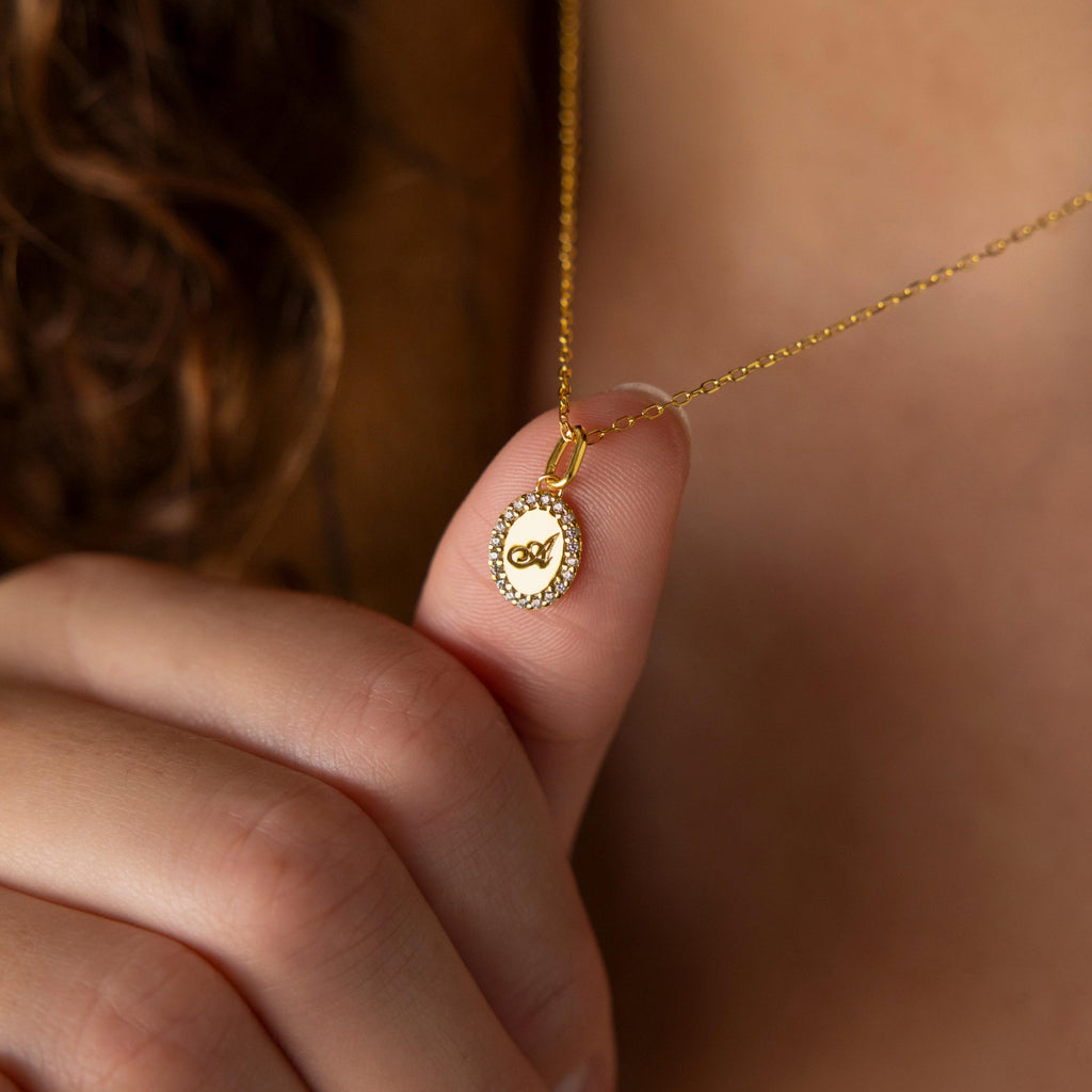 The Pave Initial Pendant Necklace features a circular pendant with an engraved letter "A," delicately held near the neck—a chic, personalized accessory ideal for everyday wear.