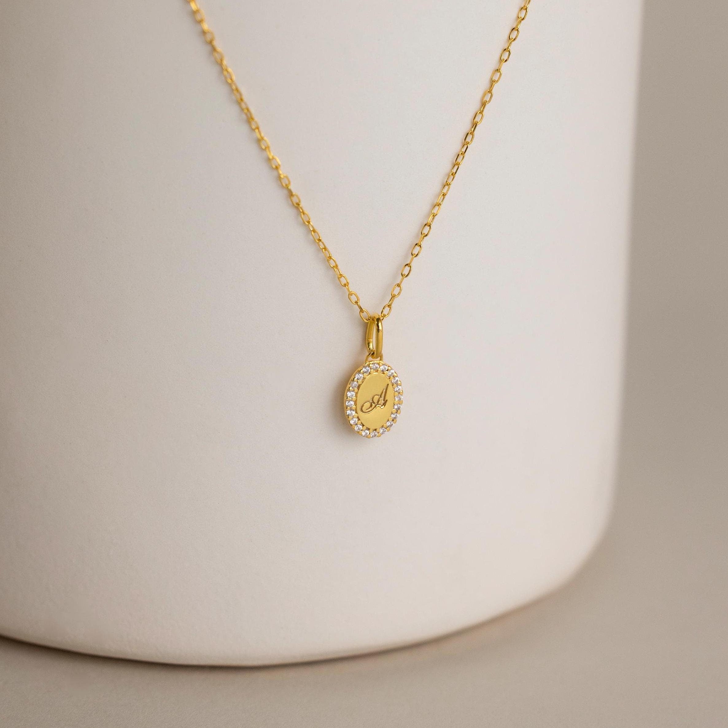 The Pave Initial Pendant Necklace features a round pendant engraved with the letter A, bordered by sparkling white stones for a personalized, elegant, and timeless look.