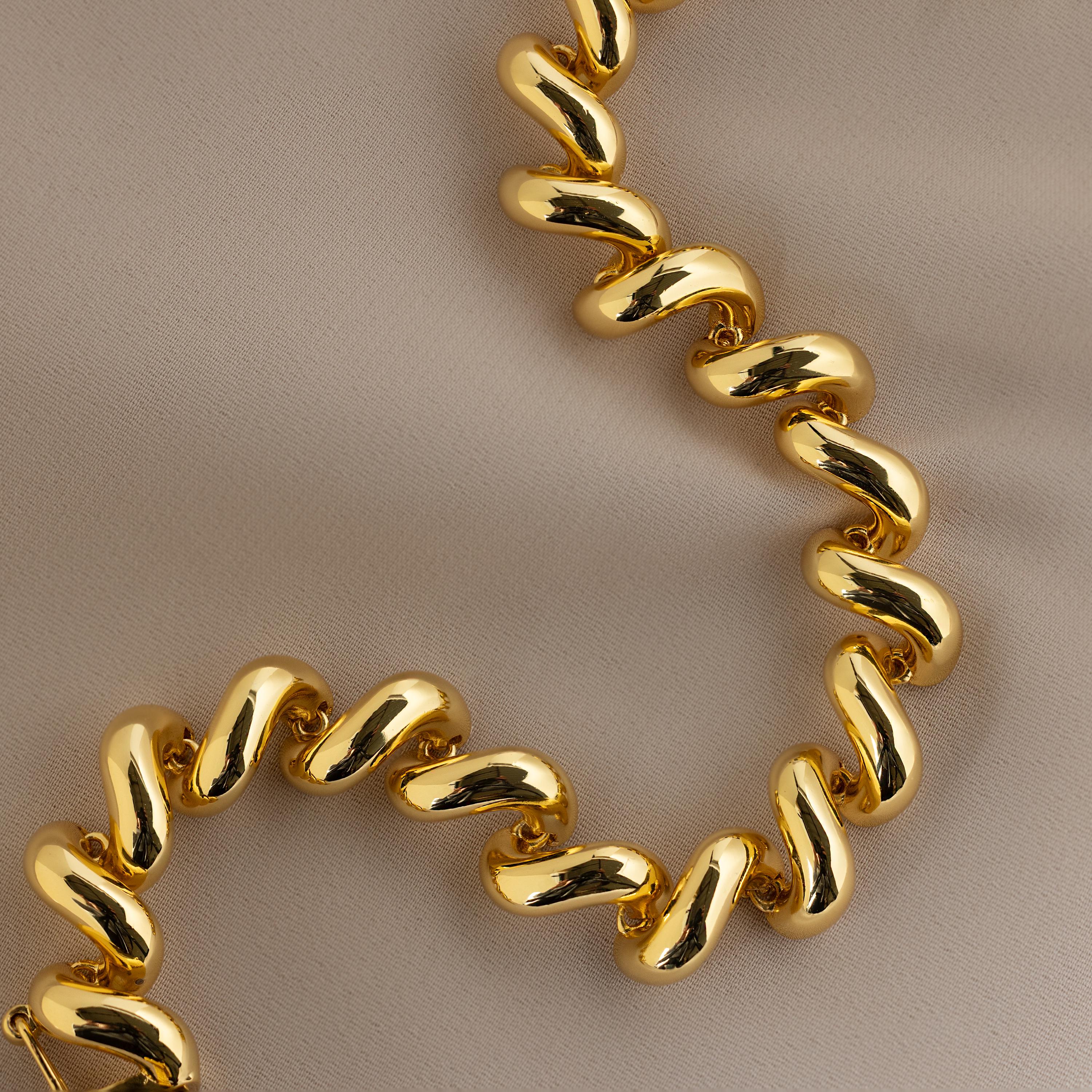 The Twisted Chain Bracelet in 18K Gold, with bold shining links displayed on smooth beige fabric, adds effortless glamour to any look.