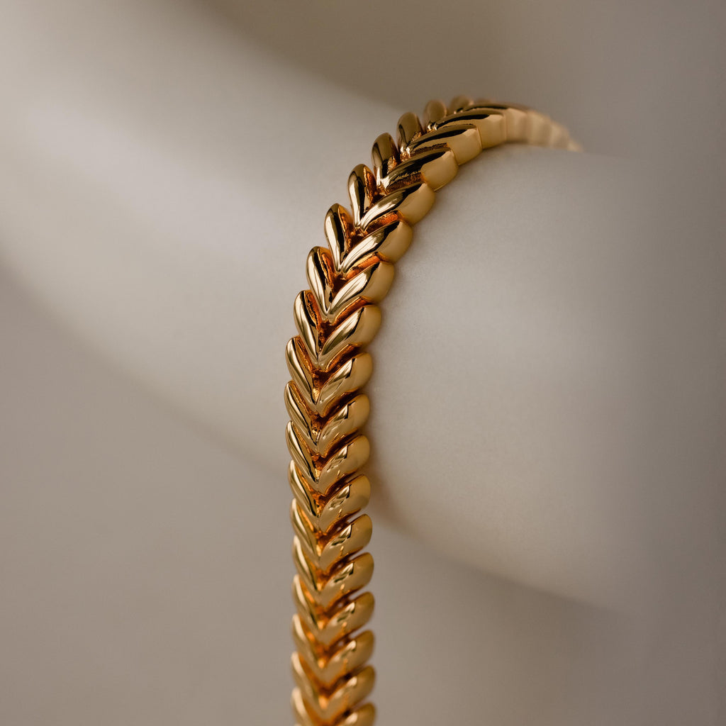 A close-up of the V-Link Chain Tennis Bracelet, featuring sculptural gold links, displayed on a light-colored surface.