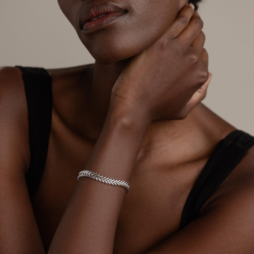 A woman in a black top rests her hand on her neck, showcasing the V-Link Chain Tennis Bracelet in silver with sculptural links.
