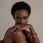 Woman with short curly hair in a black top rests her hand on her face, looking at the camera while showcasing the Dome Cuff Bracelet for a chic, stylish accent.