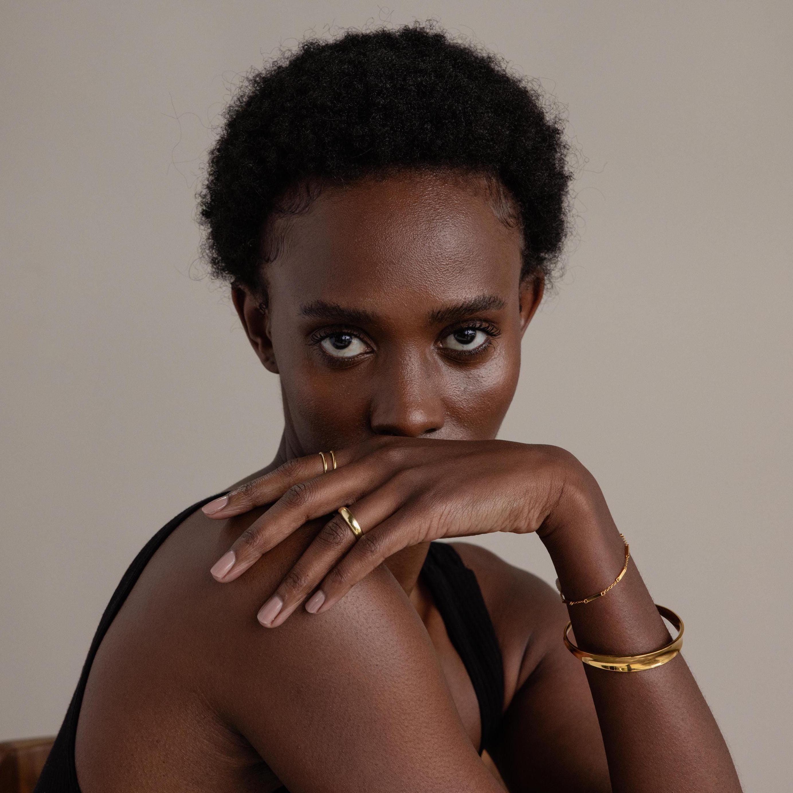Woman with short curly hair in a black top rests her hand on her face, looking at the camera while showcasing the Dome Cuff Bracelet for a chic, stylish accent.
