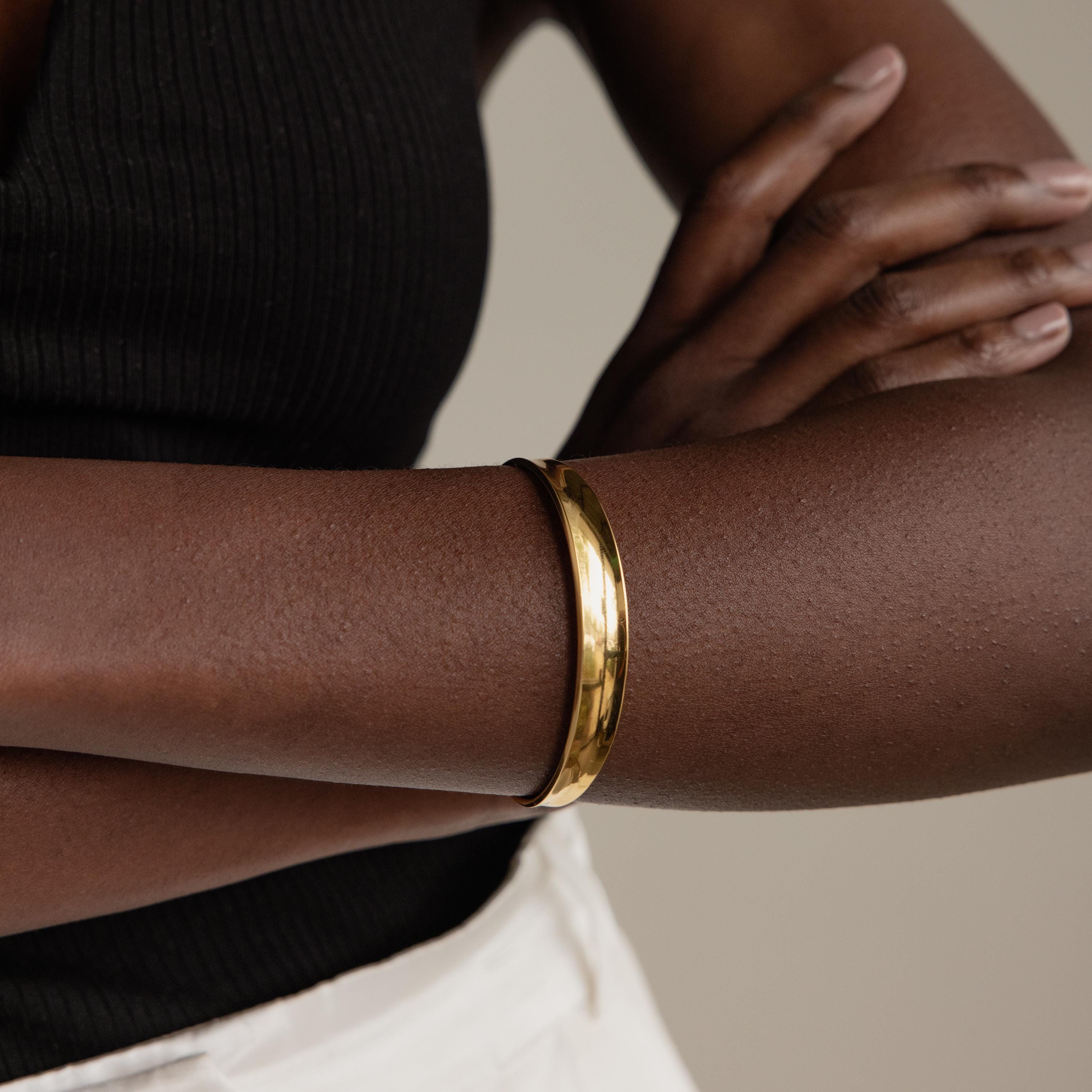 A person styles the Dome Cuff Bracelet with arms crossed, pairing it with a black top and white pants for a chic accent.